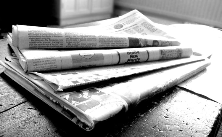 A black and white photo of a stack of newspapers on a weathered wooden surface.