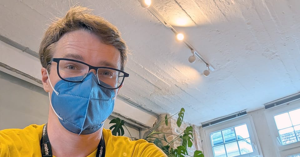 A selfie of Robin at Matrix Conf 2024 wearing a blue KN95 mask indoors.